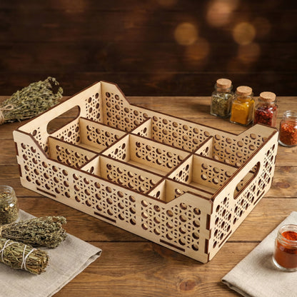 Laser cut plywood organizer tray with multiple sections shown in a kitchen context. It holds dried herbs and sits next to small glass spice jars on a dark wood surface, highlighting its use as a functional kitchen storage piece