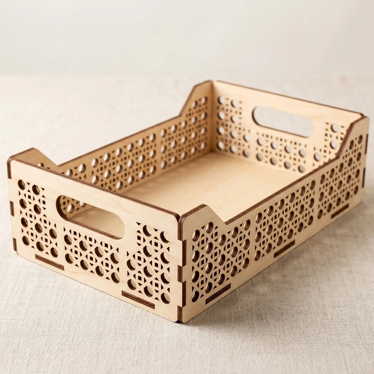 Three-quarter view of an empty single-compartment laser cut plywood tray with geometric cutout patterns on a tablecloth.