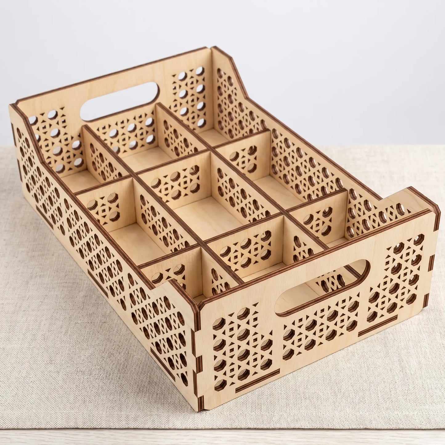 High-angle view of an empty laser cut plywood multi-compartment organizer tray sitting on a textured grey tablecloth.