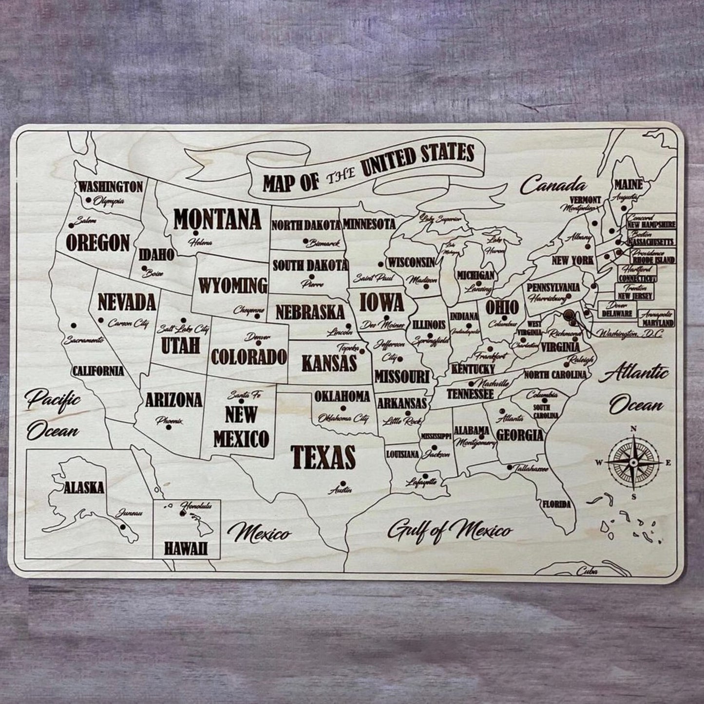 A fully assembled USA puzzle map crafted from laser cut plywood. Every state piece is fitted into the natural wood base, showing bold engraved state names, capitals, and surrounding geographic labels like the Pacific and Atlantic Oceans.