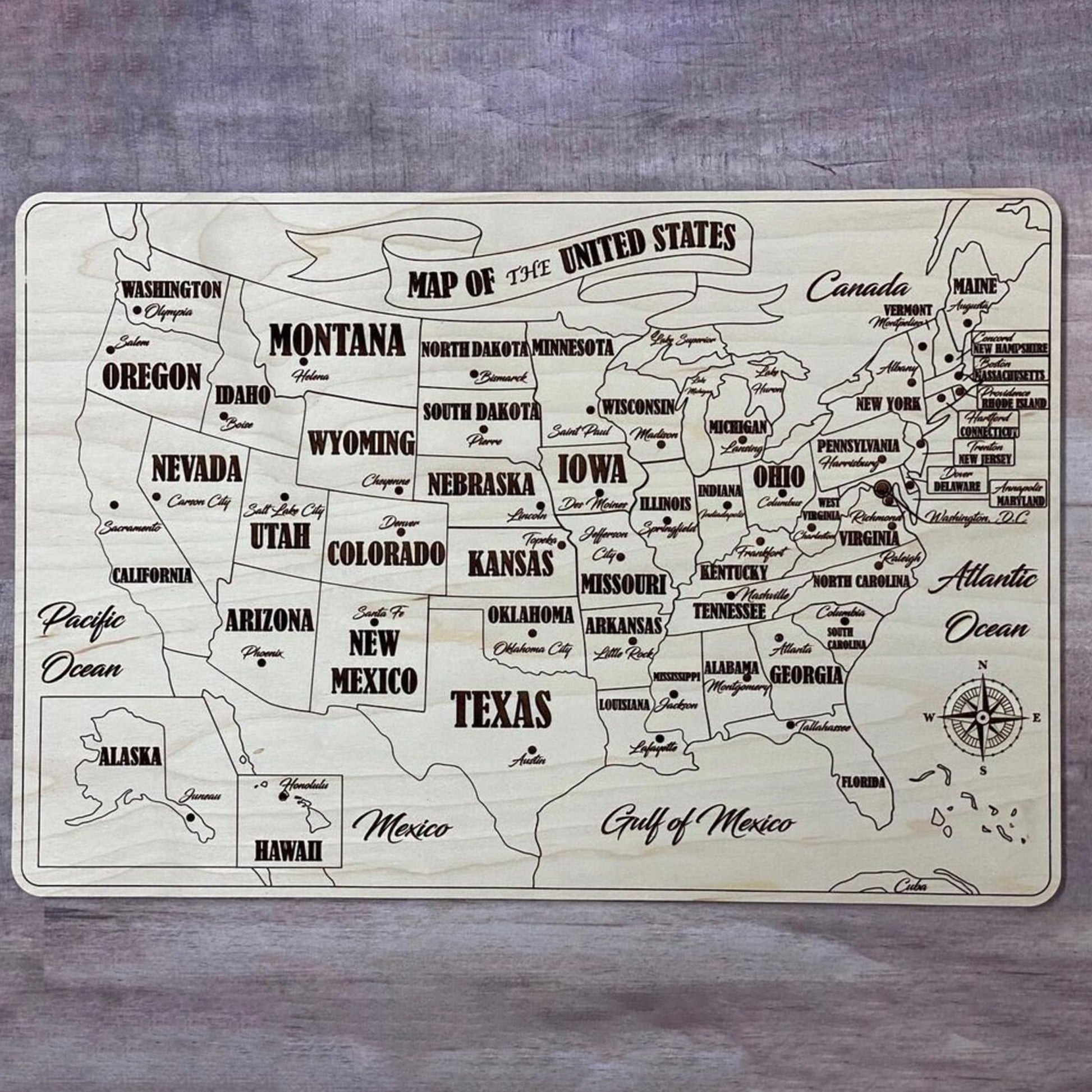 A fully assembled USA puzzle map crafted from laser cut plywood. Every state piece is fitted into the natural wood base, showing bold engraved state names, capitals, and surrounding geographic labels like the Pacific and Atlantic Oceans.