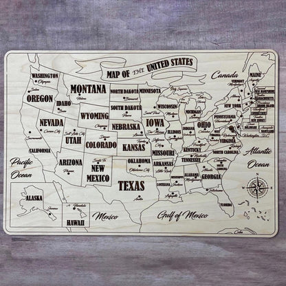 A fully assembled USA puzzle map crafted from laser cut plywood. Every state piece is fitted into the natural wood base, showing bold engraved state names, capitals, and surrounding geographic labels like the Pacific and Atlantic Oceans.