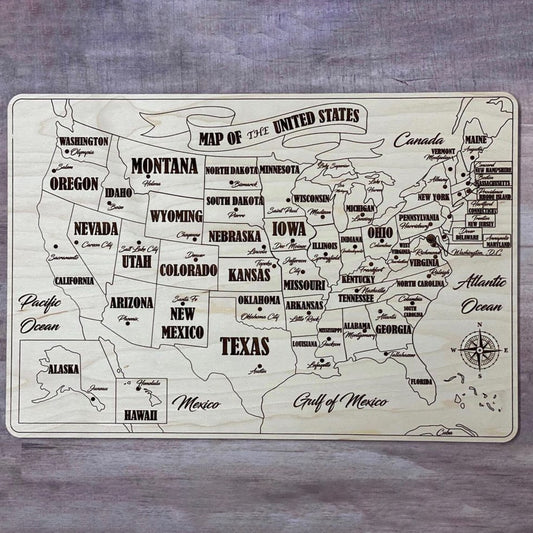 A fully assembled USA puzzle map crafted from laser cut plywood. Every state piece is fitted into the natural wood base, showing bold engraved state names, capitals, and surrounding geographic labels like the Pacific and Atlantic Oceans.