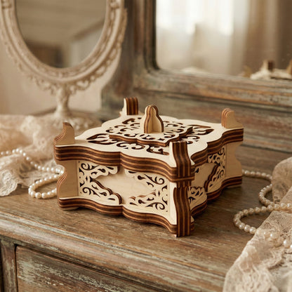 Ornate vintage-style jewelry box crafted from laser cut plywood. Features intricate filigree cutouts on the lid and sides with a decorative handle. Resting on a rustic dresser next to a pearl necklace and lace.