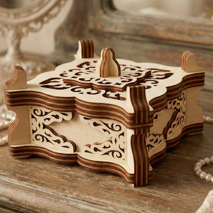 Ornate vintage-style jewelry box crafted from laser cut plywood. Features intricate filigree cutouts on the lid and sides with a decorative handle. Resting on a rustic dresser next to a pearl necklace and lace.