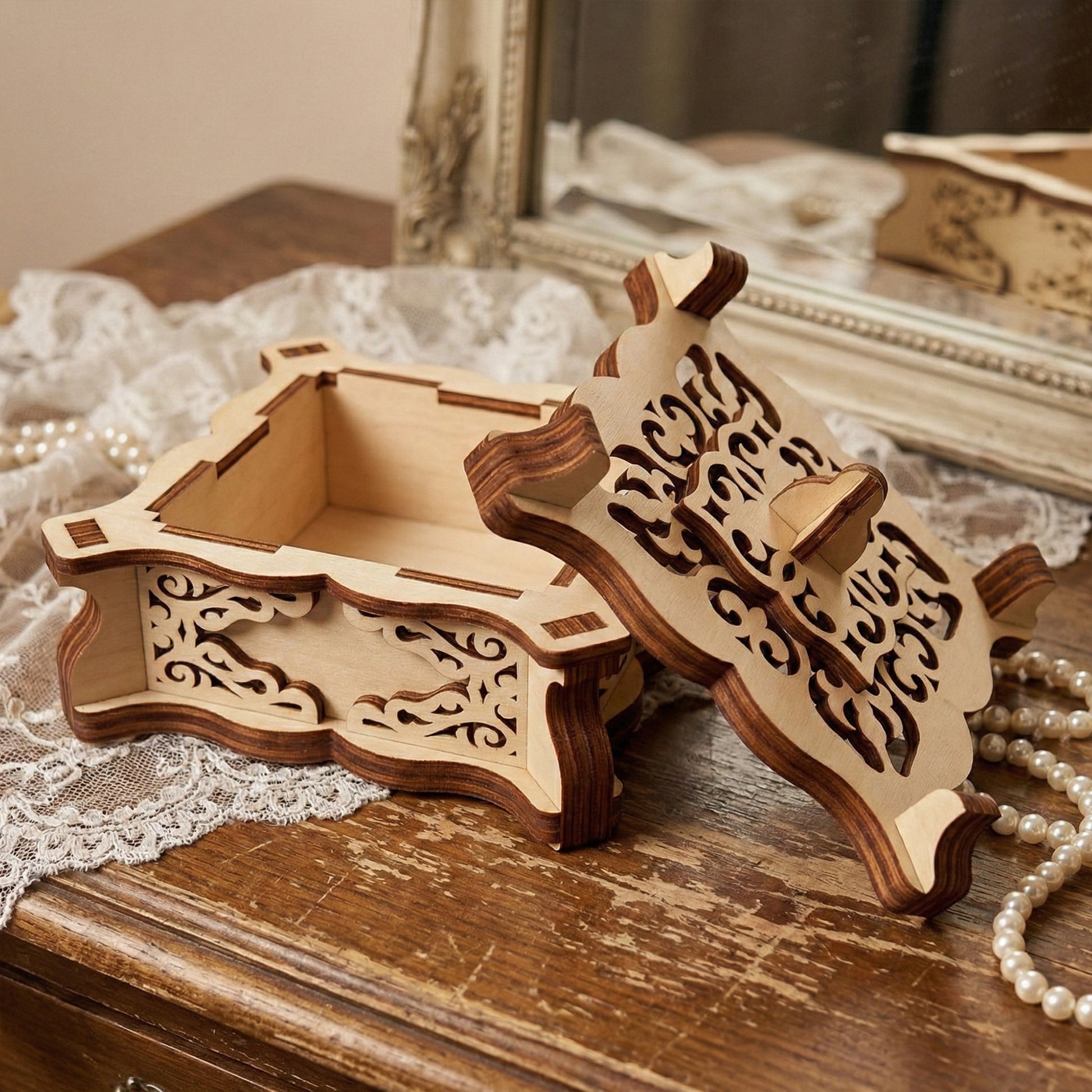 Open view of a laser cut plywood vintage jewelry box, revealing the empty interior. The lid is propped up to show the detailed scrollwork and dark burnt edges. Displayed on a wooden surface with pearls and a vanity mirror.