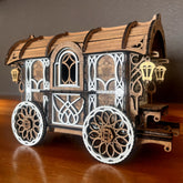 A laser cut wooden model of a Nomad Caravan Wagon with intricate geometric patterns and moving wheels, displayed on a wooden surface.