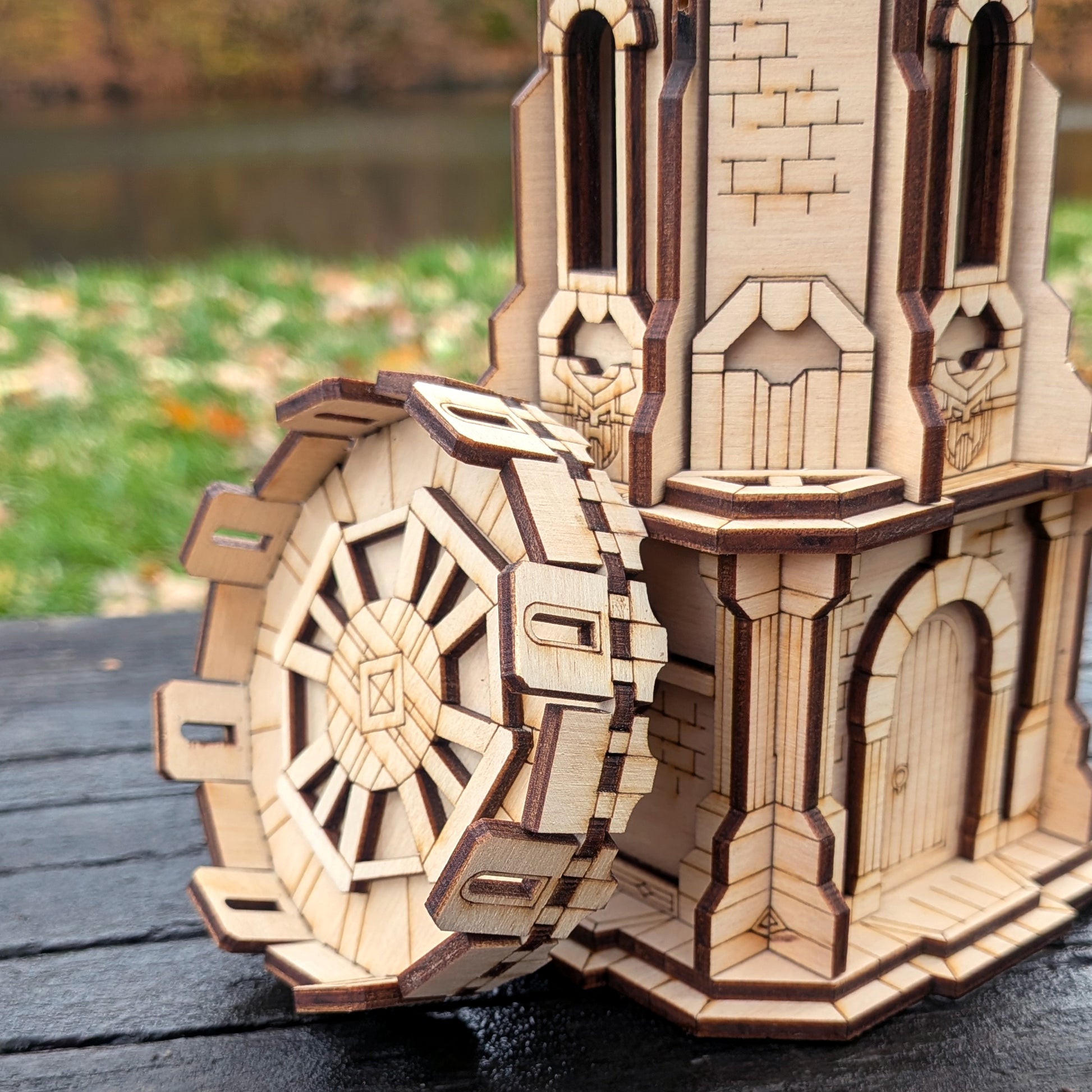 Wooden laser cut model of a castle with a large gear on a wooden surface.