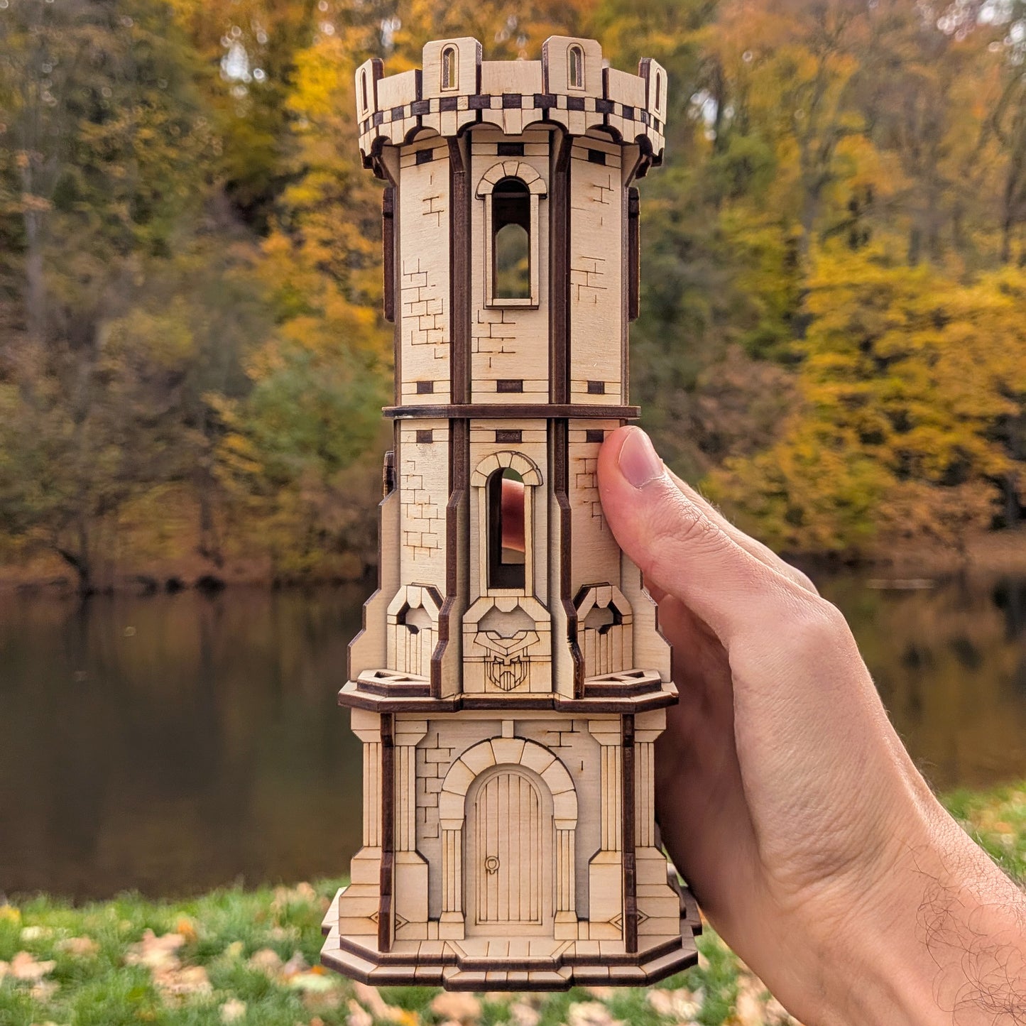 Wooden laser cut model of a castle tower held by a hand with a scenic background
