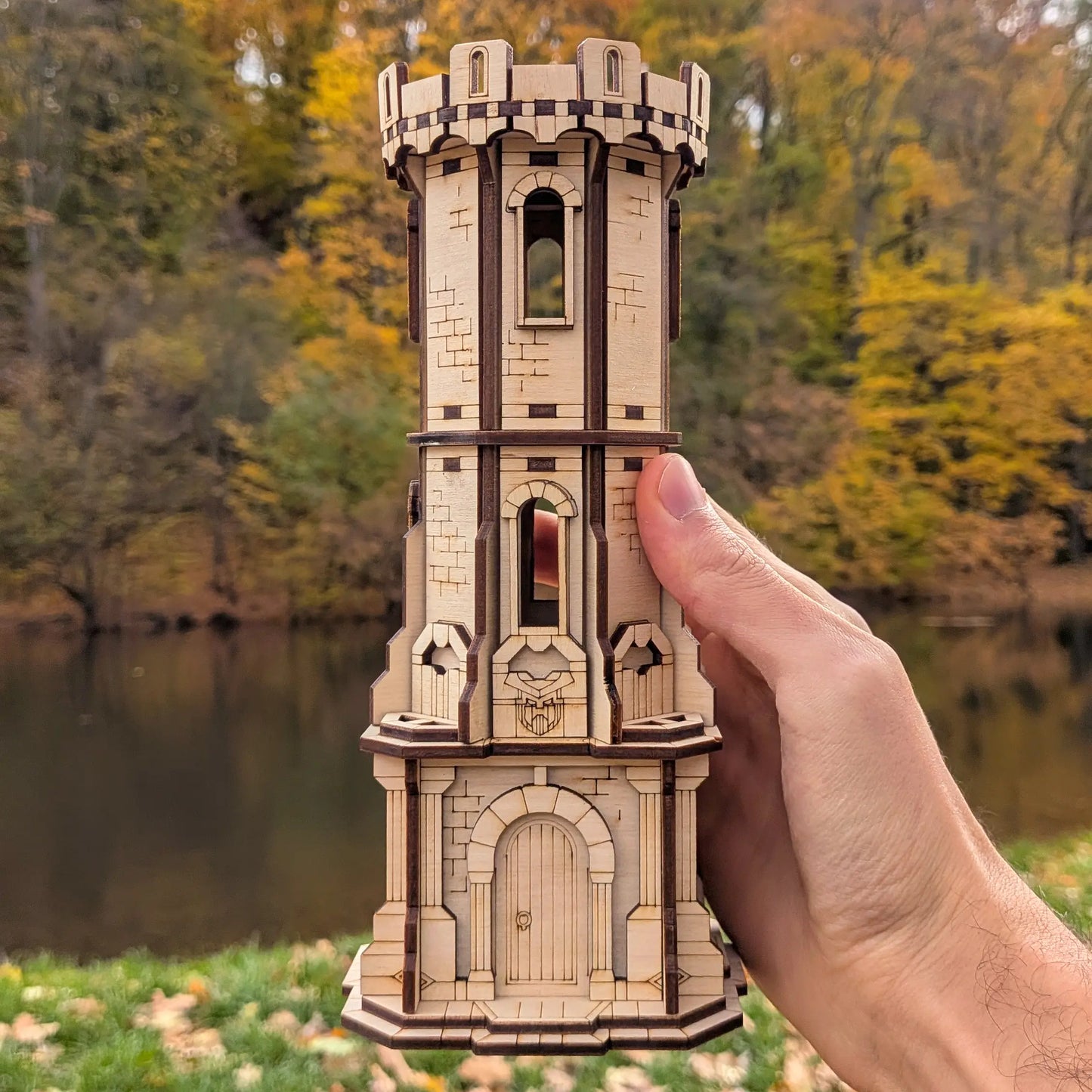 A side angle view of a person's hand holding a detailed multi-tier miniature RPG gaming watchtower in laser cut plywood