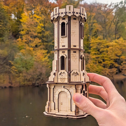 Hand holding a miniature laser cut castle model against a natural background with trees and water.
