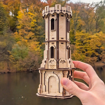 A human hand carefully holding up a highly detailed miniature medieval castle watchtower model made from laser cut plywood