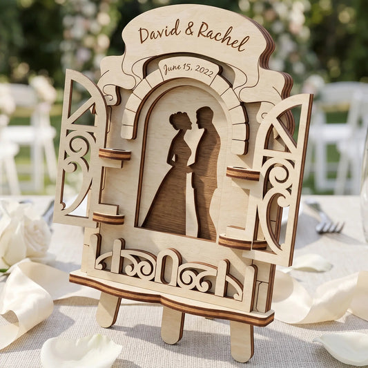 Laser cut plywood wedding window decor with open shutters showing a couple's silhouette and personalized names on a table.