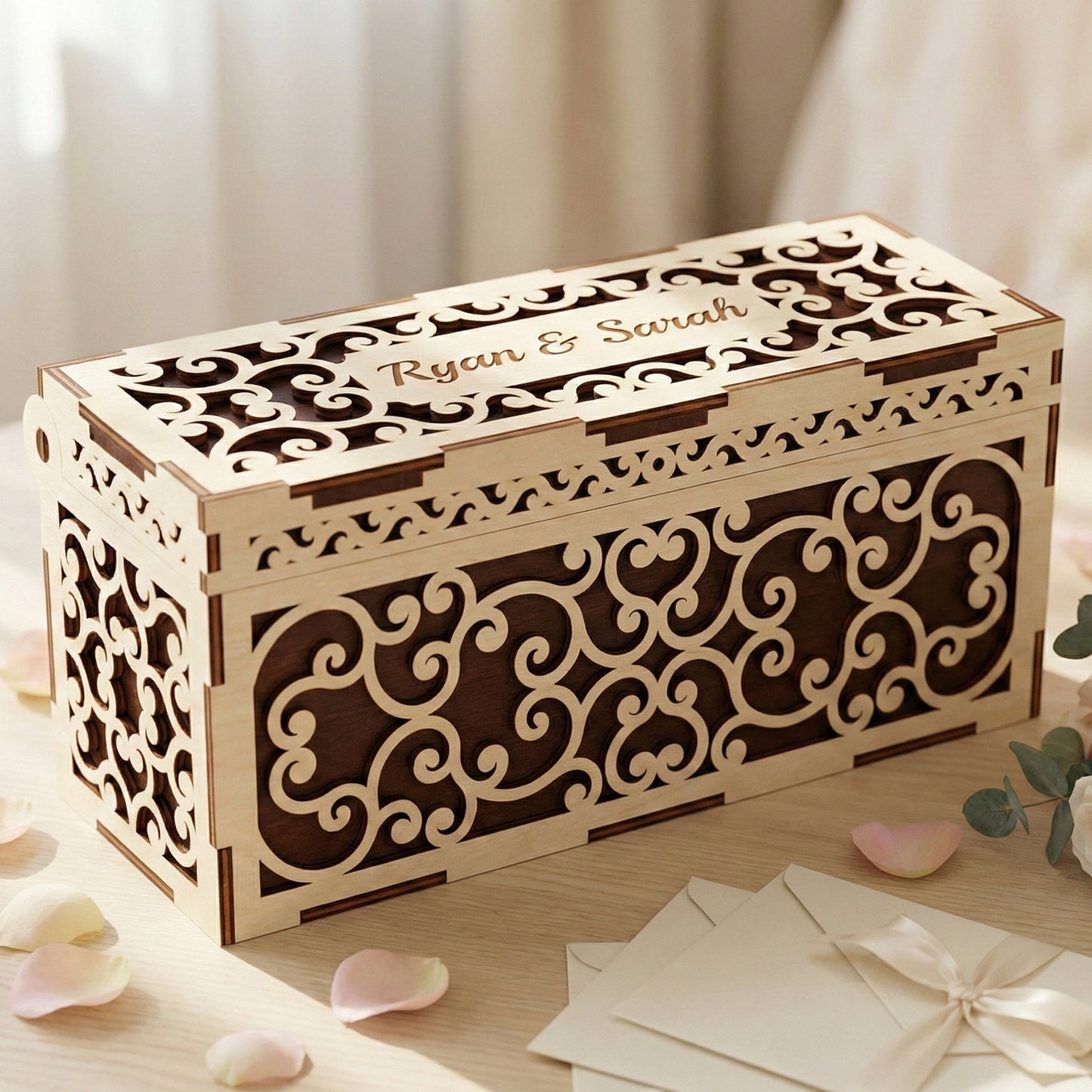 Elegant wedding wish box made of laser cut plywood with intricate scrollwork patterns. The lid is engraved with "Ryan & Sarah." The box features a dark wood interior visible through light plywood cutouts, set on a table with rose petals.