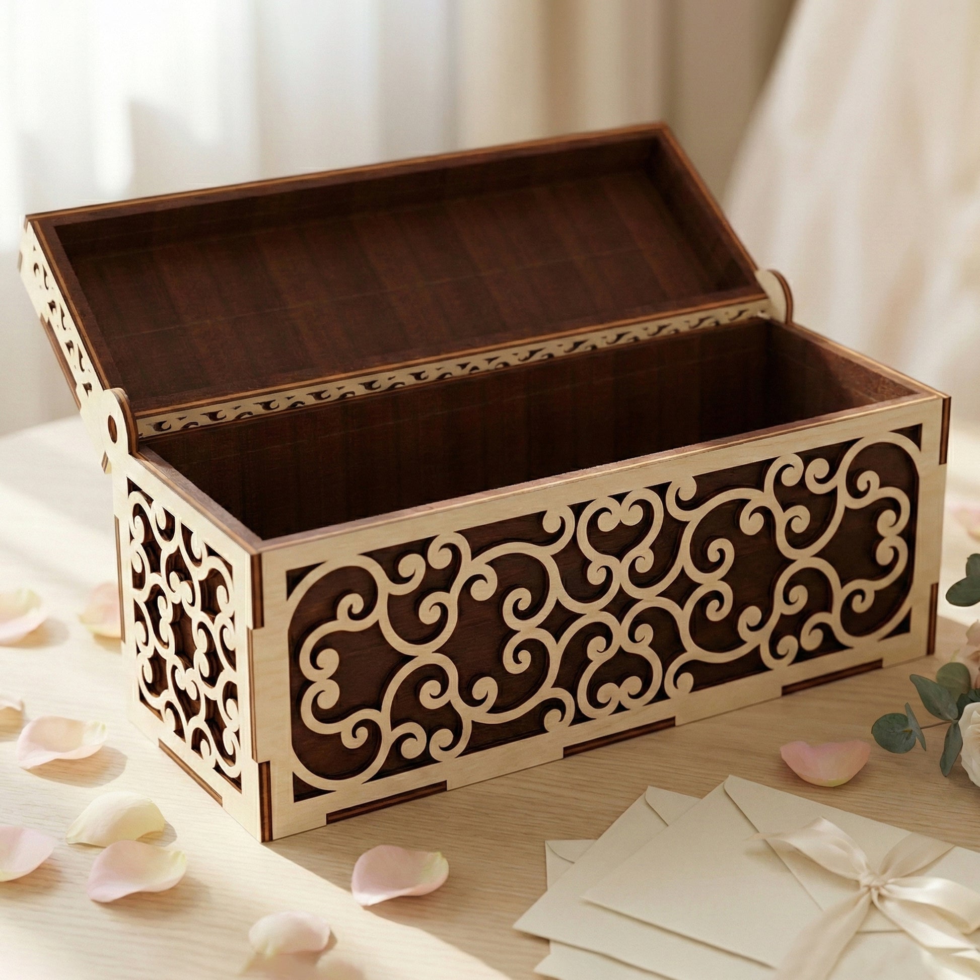 An open wooden wedding card box crafted from laser cut plywood. The interior reveals a deep brown wood finish, while the exterior shows delicate cream-colored filigree. Placed next to envelopes and a ribbon, highlighting its large capacity.