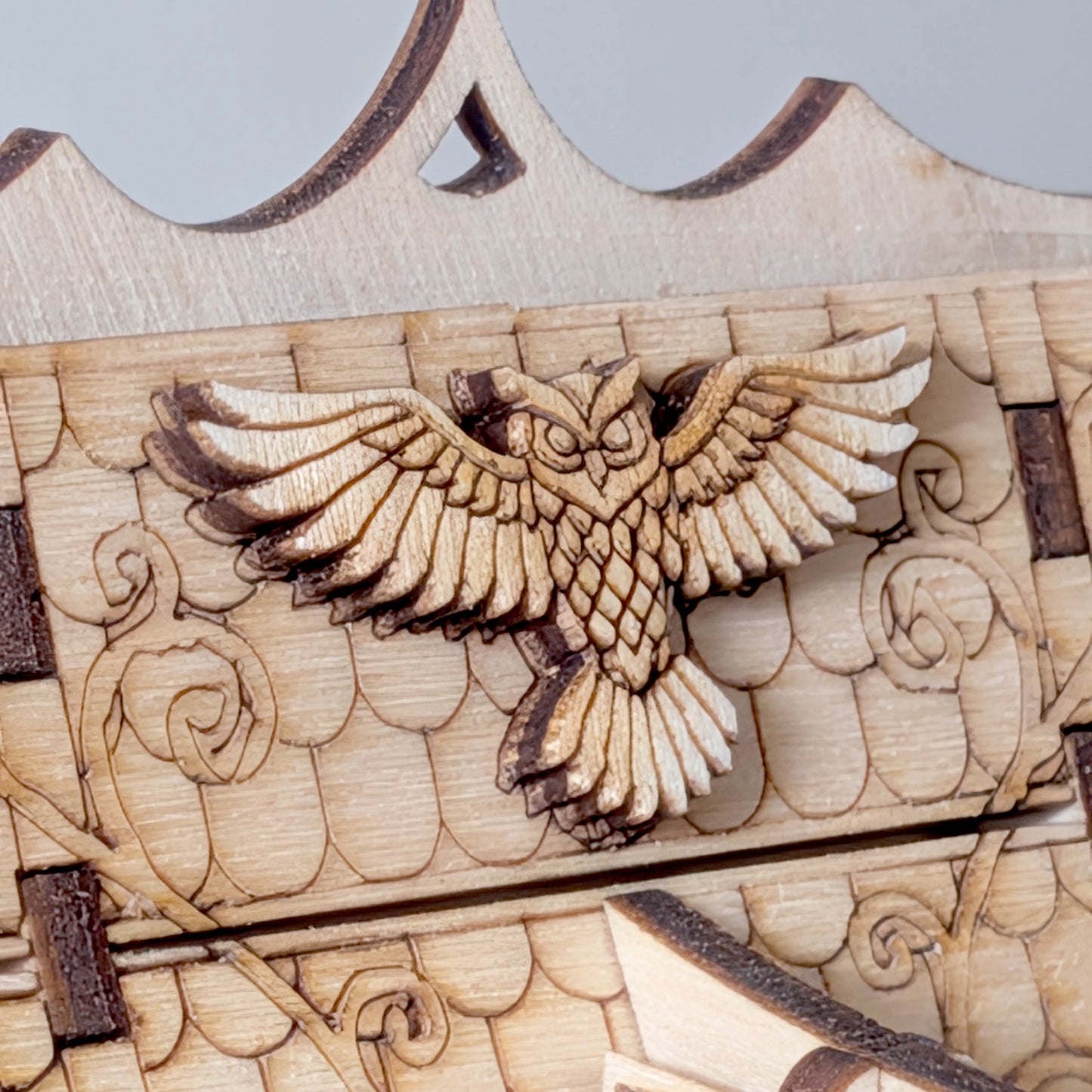 Close-up of a laser cut wooden owl decoration mounted on the roof of the fairy house, showing detailed engraved feathers and textured shingles.