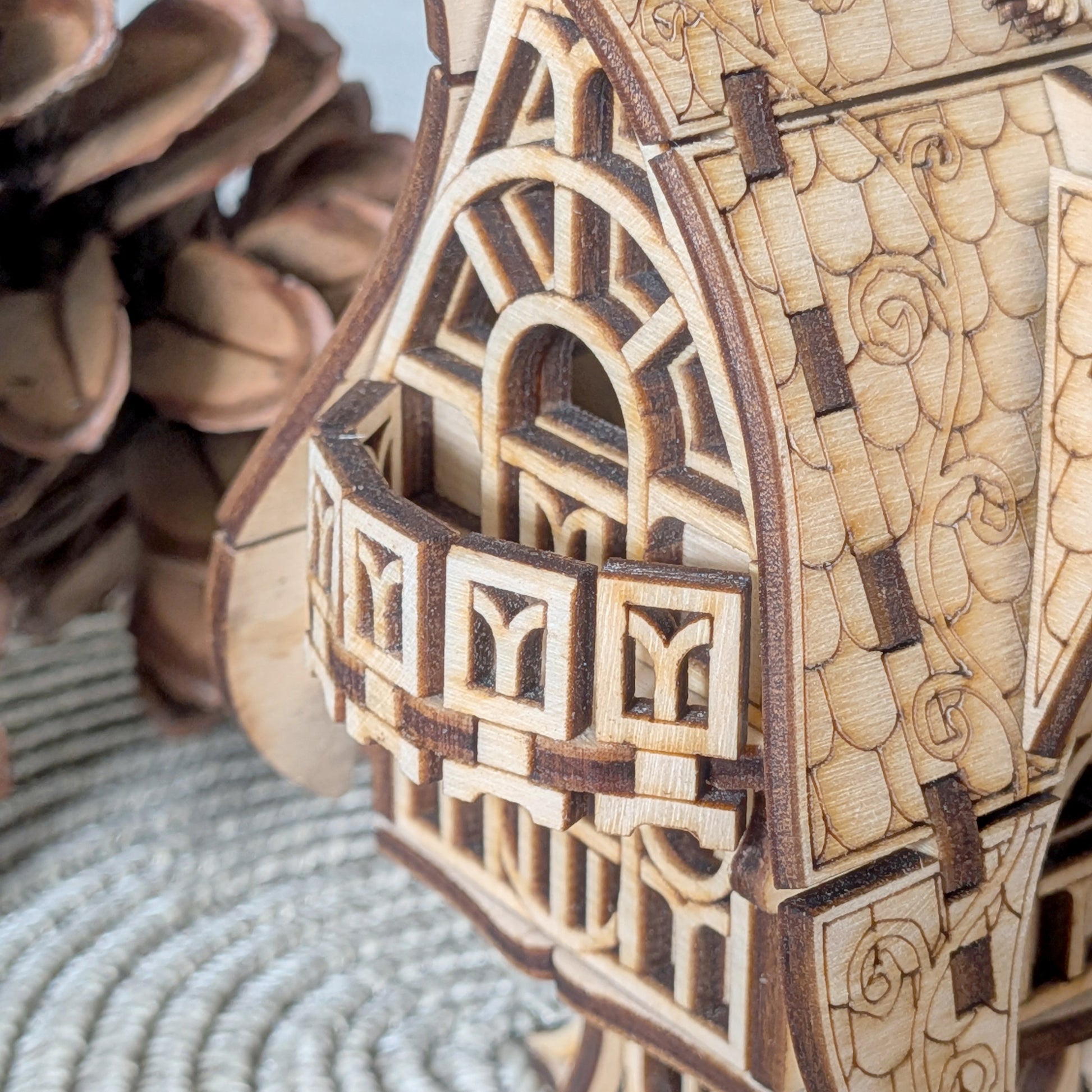 Close-up of the balcony section of the laser cut wooden house, showing layered wood pieces, carved arches, and detailed decorative trim.