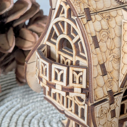 A detailed macro close-up showcasing the tiny curved balcony and window profiles of a laser cut plywood fantasy cottage.