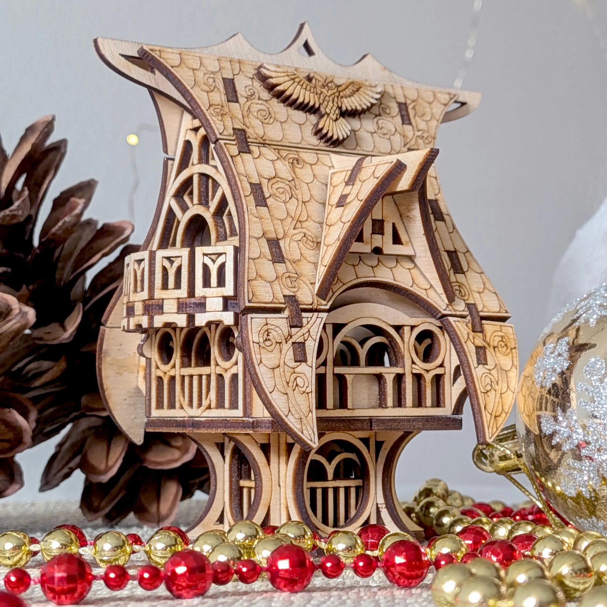 Atmospheric close-up shot of a whimsical miniature fairytale owl house in laser cut plywood, staged with red holiday beads.