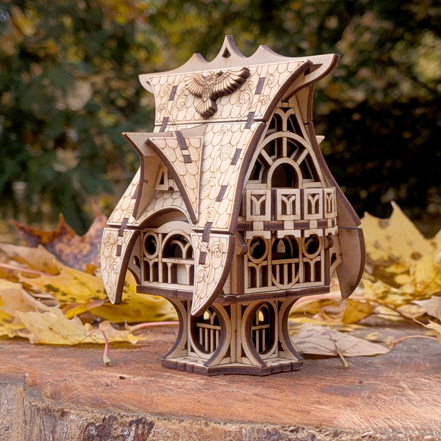 Laser cut wooden fairy house model with curved roof and engraved owl detail, displayed outdoors on a tree stump surrounded by autumn leaves.