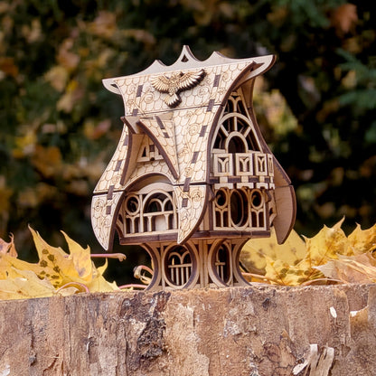 Laser cut wooden fairy house shown outdoors on a tree stump surrounded by autumn leaves, highlighting its carved windows and curved roof.