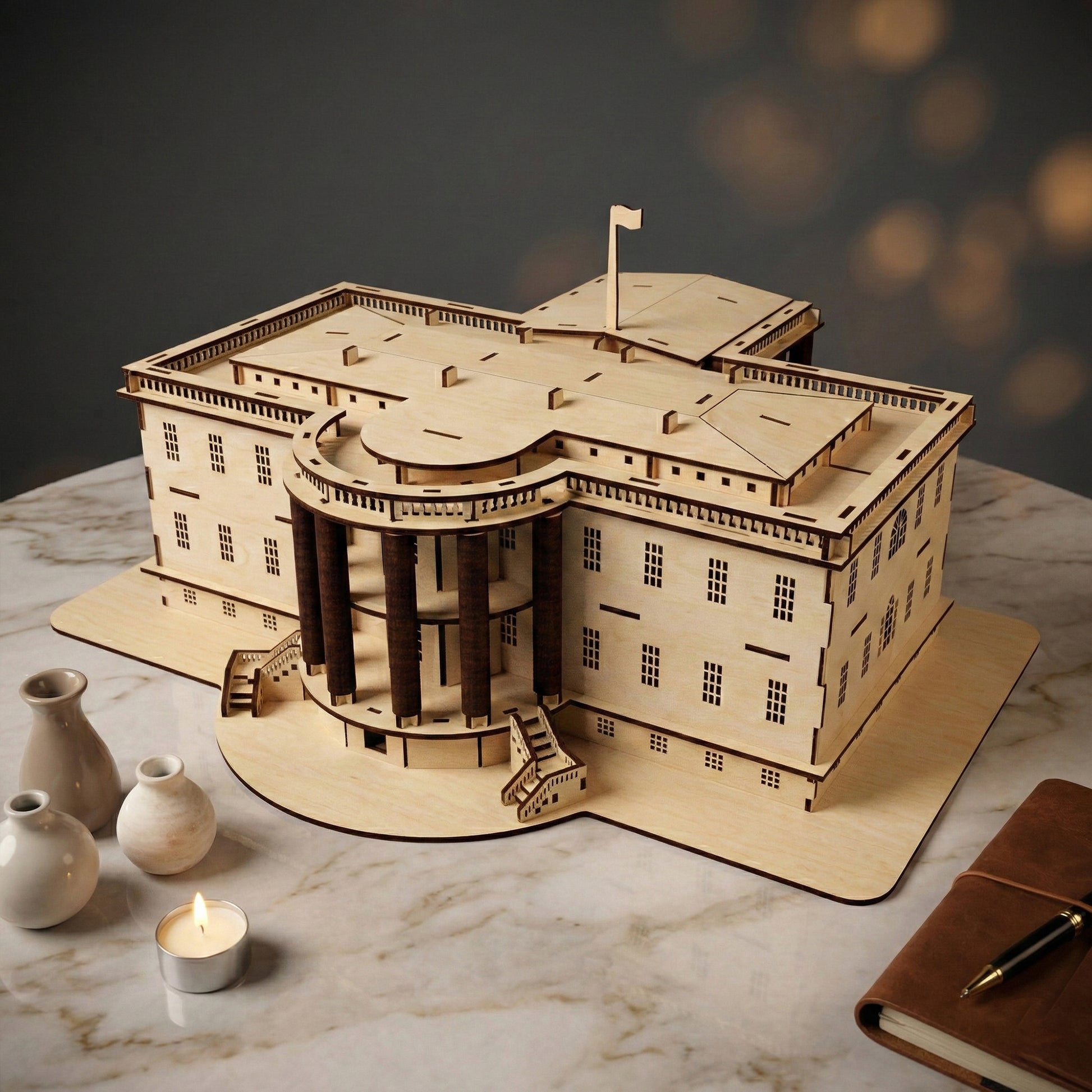 Perspective view of the laser cut plywood White House, highlighting the 3D construction and layered roof details. The natural wood grain is visible. Placed on marble with a leather journal and pen in the foreground for scale.