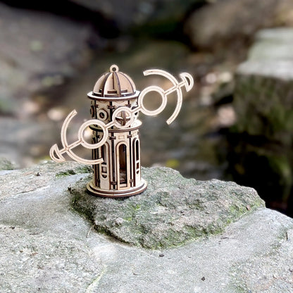 Laser cut plywood kinetic windmill toy with anchor wings tilted right, standing on a grey mossy rock near a creek.