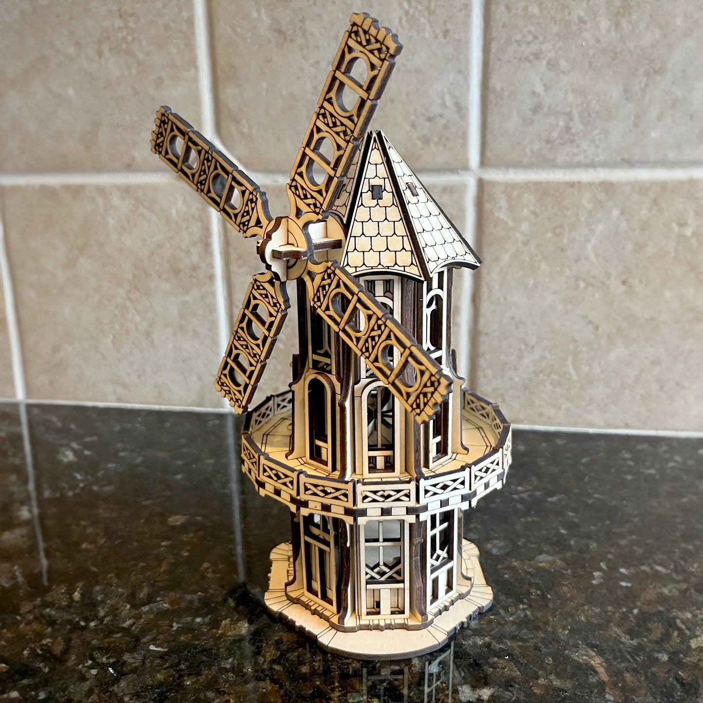 Assembled laser cut plywood Victorian windmill model shown from a high angle on a dark glossy kitchen countertop.