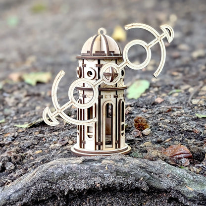 Laser cut plywood windmill tower toy with tilted anchor wings, sitting on a ground root outdoors.