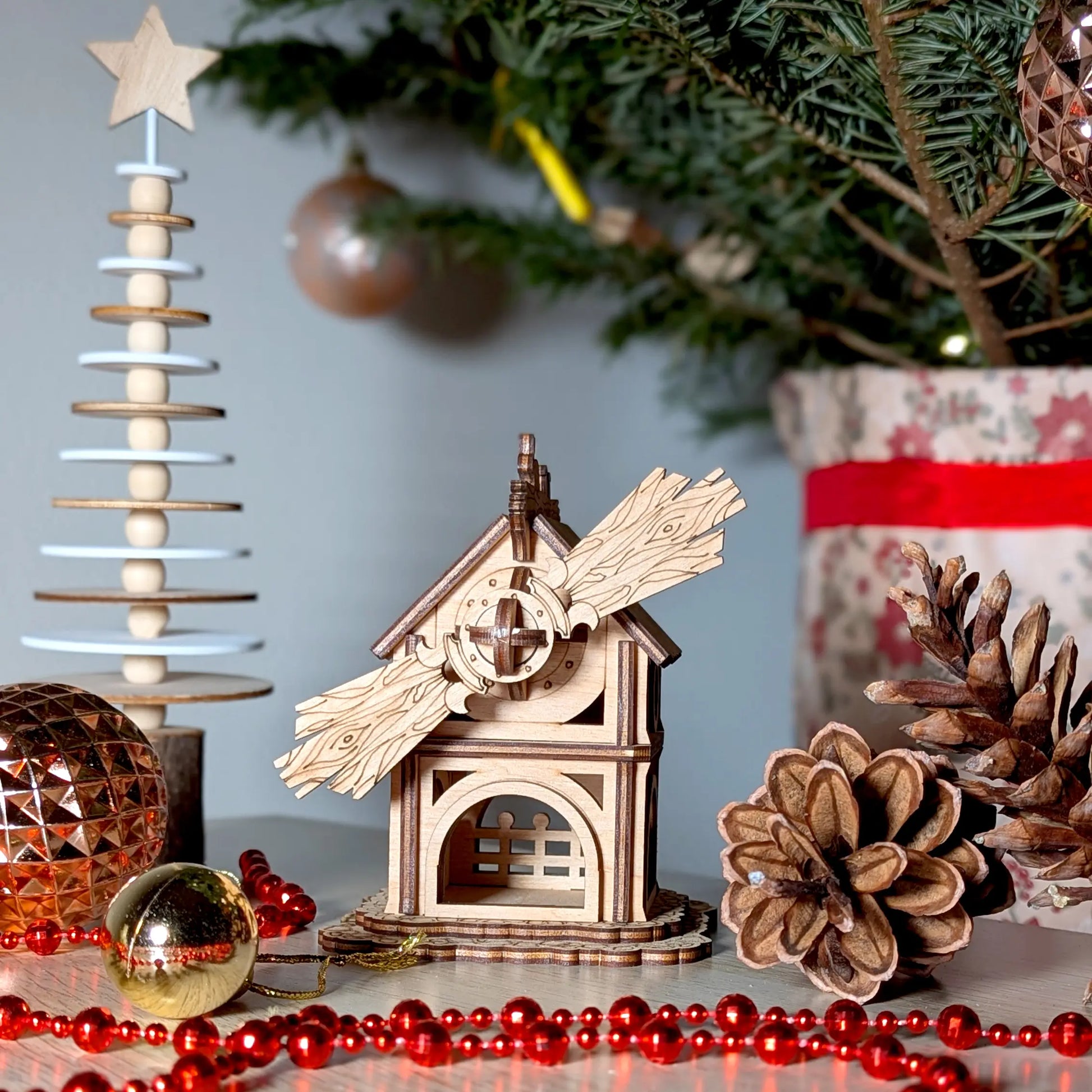 Front view of an assembled miniature holiday windmill puzzle made of laser cut plywood, staged near festive decorations.