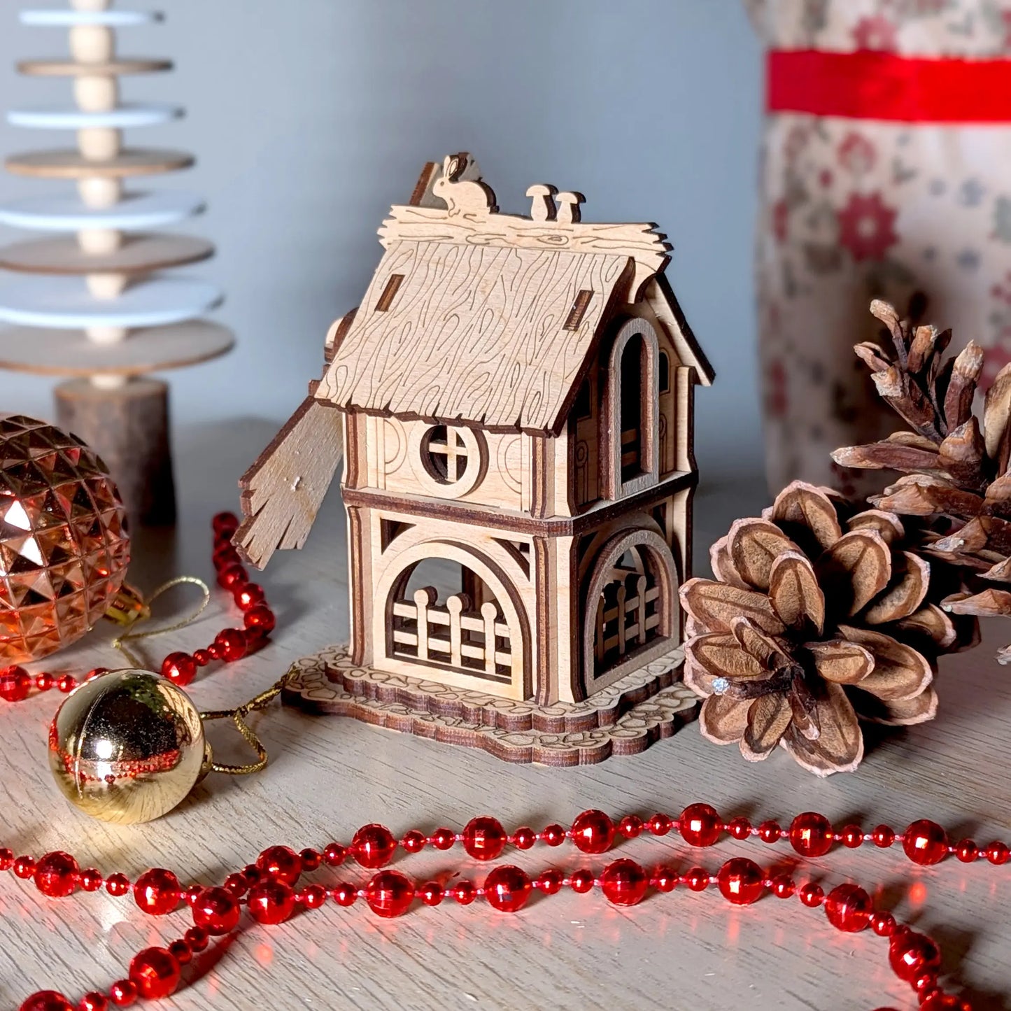 Side view of a miniature windmill with a textured thatched roof made of laser cut plywood, staged with red Christmas beads.
