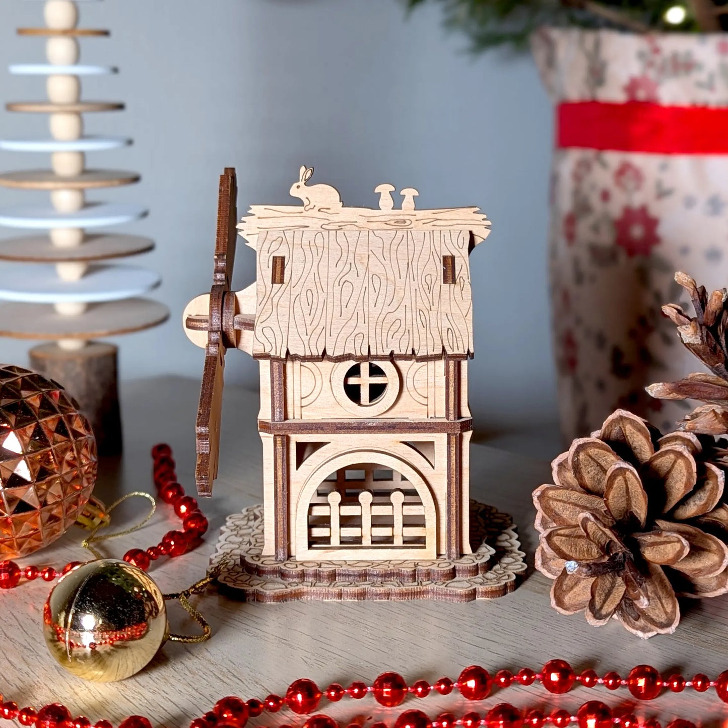 Straight side profile of a wooden toy windmill showcasing a fence and round window made from fine laser cut plywood layers.