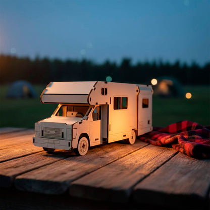 Side view of a laser cut wooden plywood truck camper model with a slide-out section, resting on a picnic table. The 3D plywood puzzle features intricate window cutouts and wheel details, set against a twilight campsite with a red plaid blanket