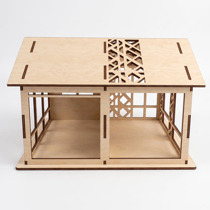 Front-facing studio view of a laser-cut birch plywood woodland dollhouse with two open rooms and patterned roof panels.