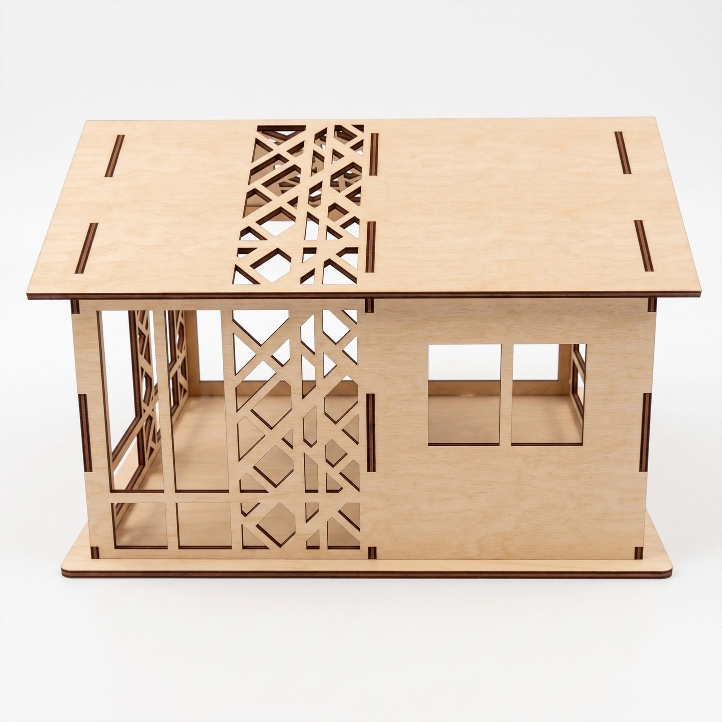 Studio view of a laser-cut birch plywood woodland dollhouse showing geometric wall patterns, windows, and dark burnt edges.