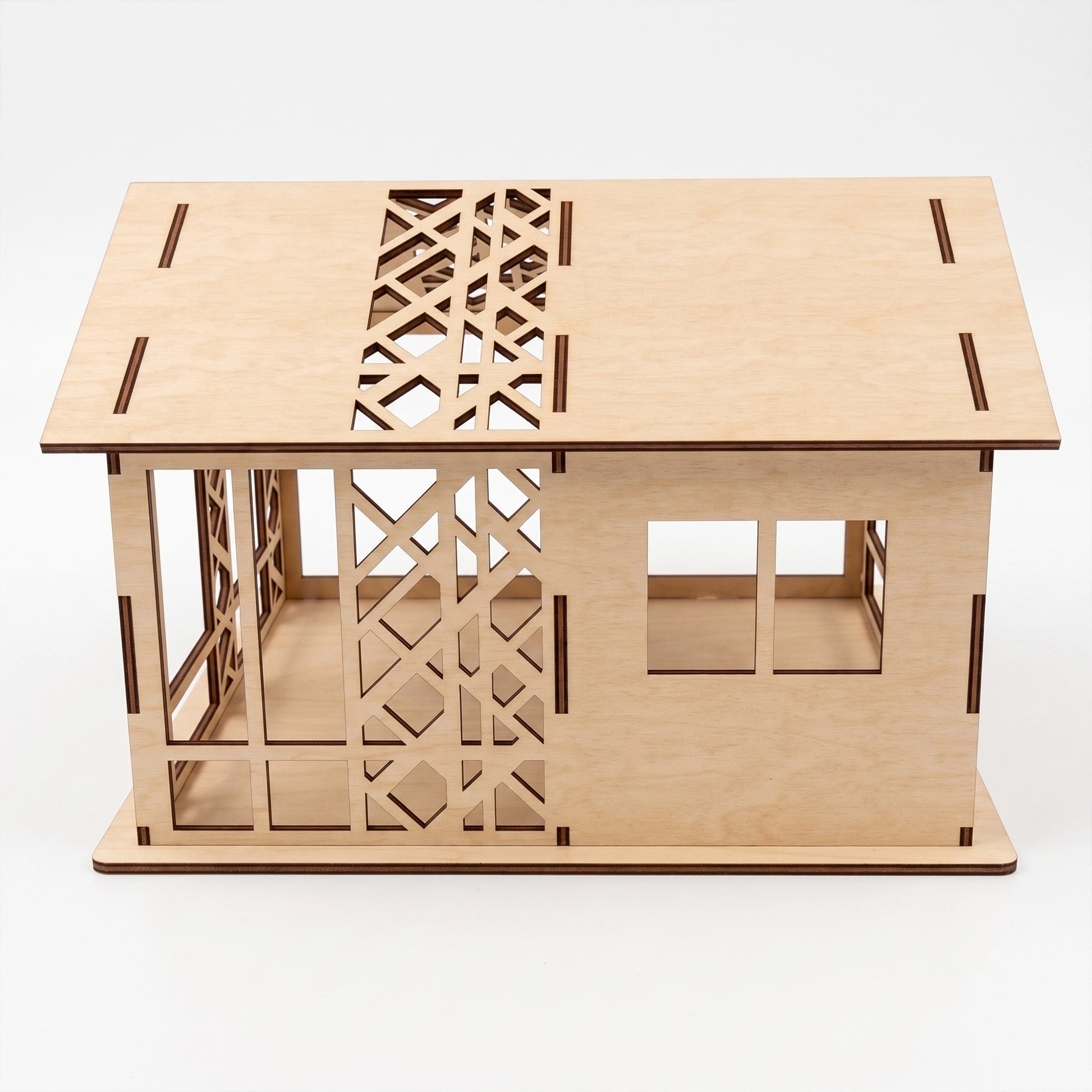 Studio view of a laser-cut birch plywood woodland dollhouse showing geometric wall patterns, windows, and dark burnt edges.
