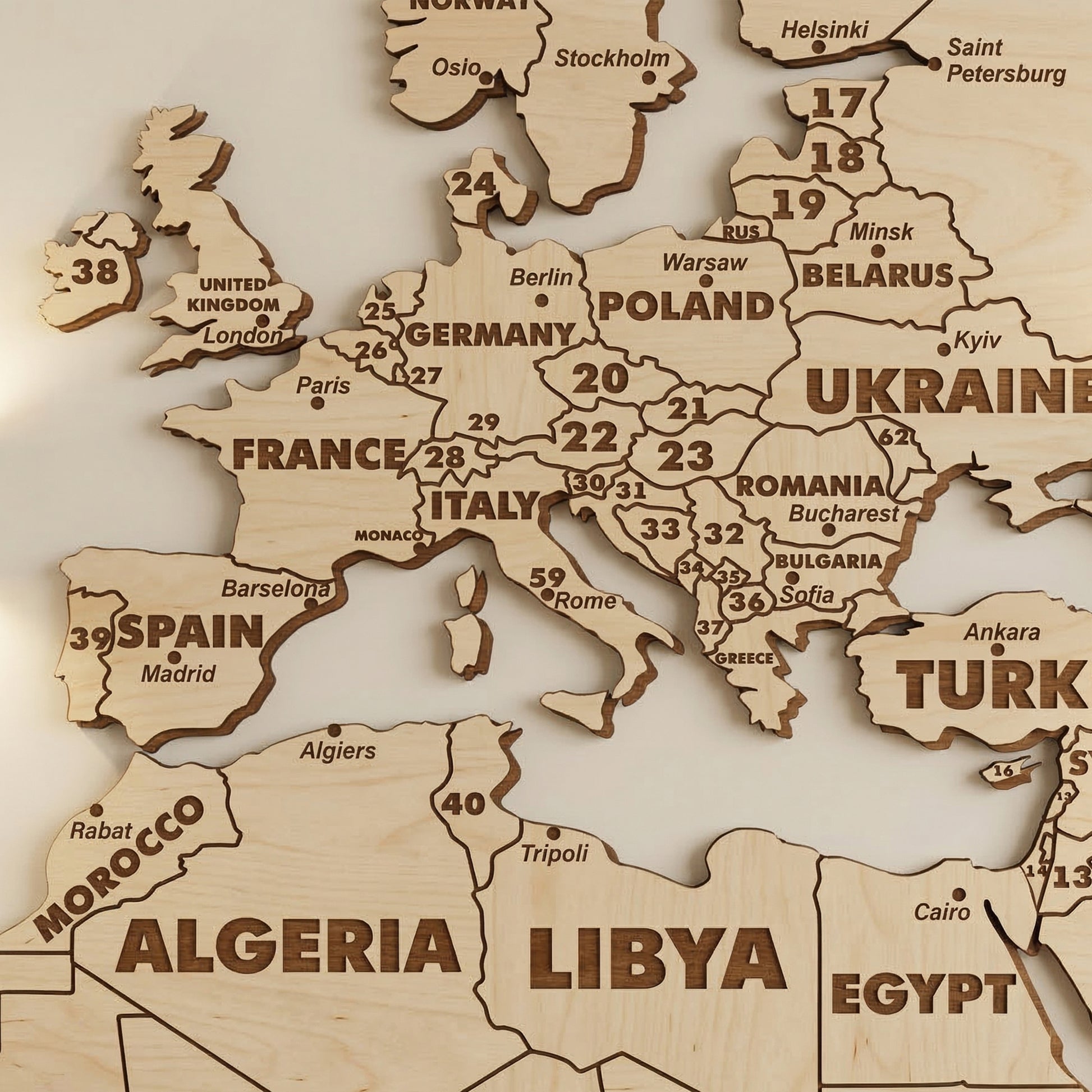 Close-up of Europe on the laser cut plywood world map. Shows detailed engraving of country names and cities like Berlin and Kyiv. Numbers represent smaller countries. Highlights precise dark burnt edges and natural light wood grain.