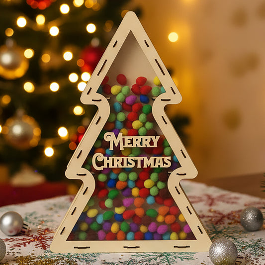 Laser cut wooden Xmas Chocolate Tree with transparent front filled with colorful chocolate balls and "Merry Christmas" engraving, displayed against a warm Christmas tree bokeh background.